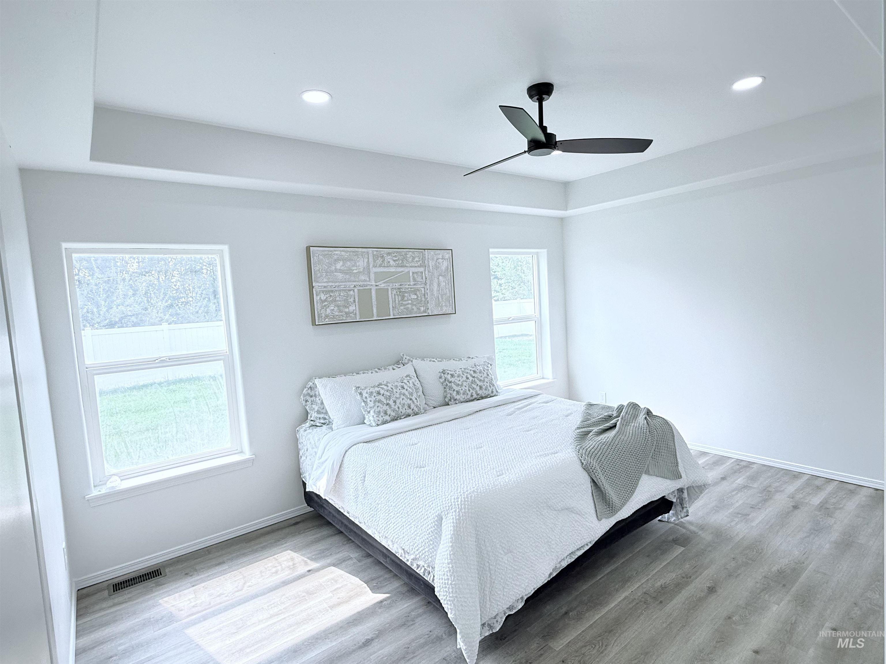 Bedroom with wood finished floors, a ceiling fan, a tray ceiling, and recessed lighting