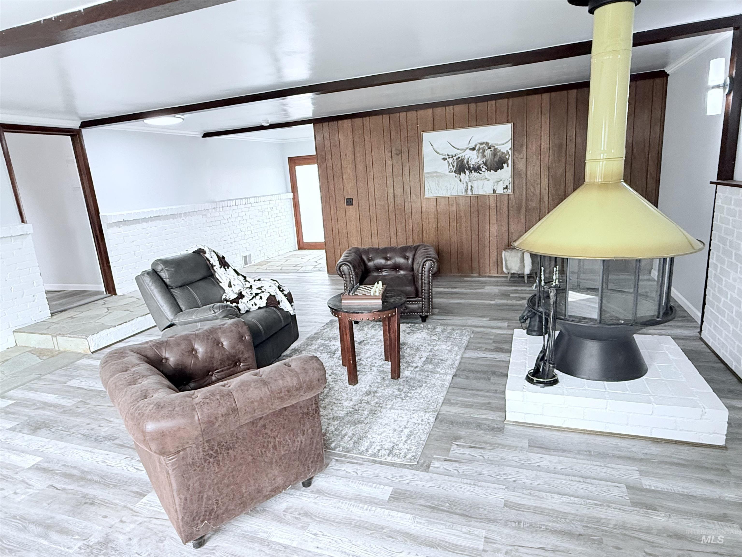 Living room with a wainscoted wall, wood finished floors, wood walls, beamed ceiling, and ornamental molding