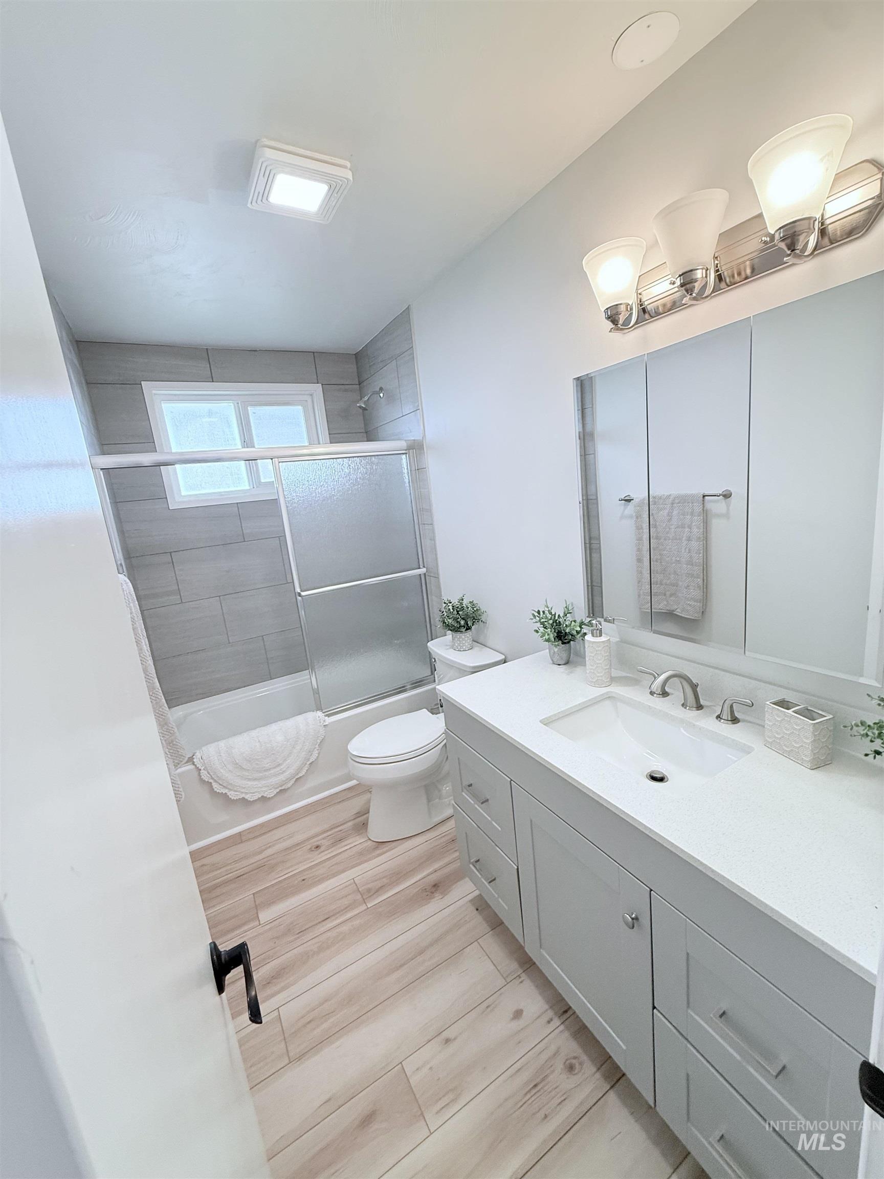 Bathroom featuring bath / shower combo with glass door, vanity, and light wood-type flooring