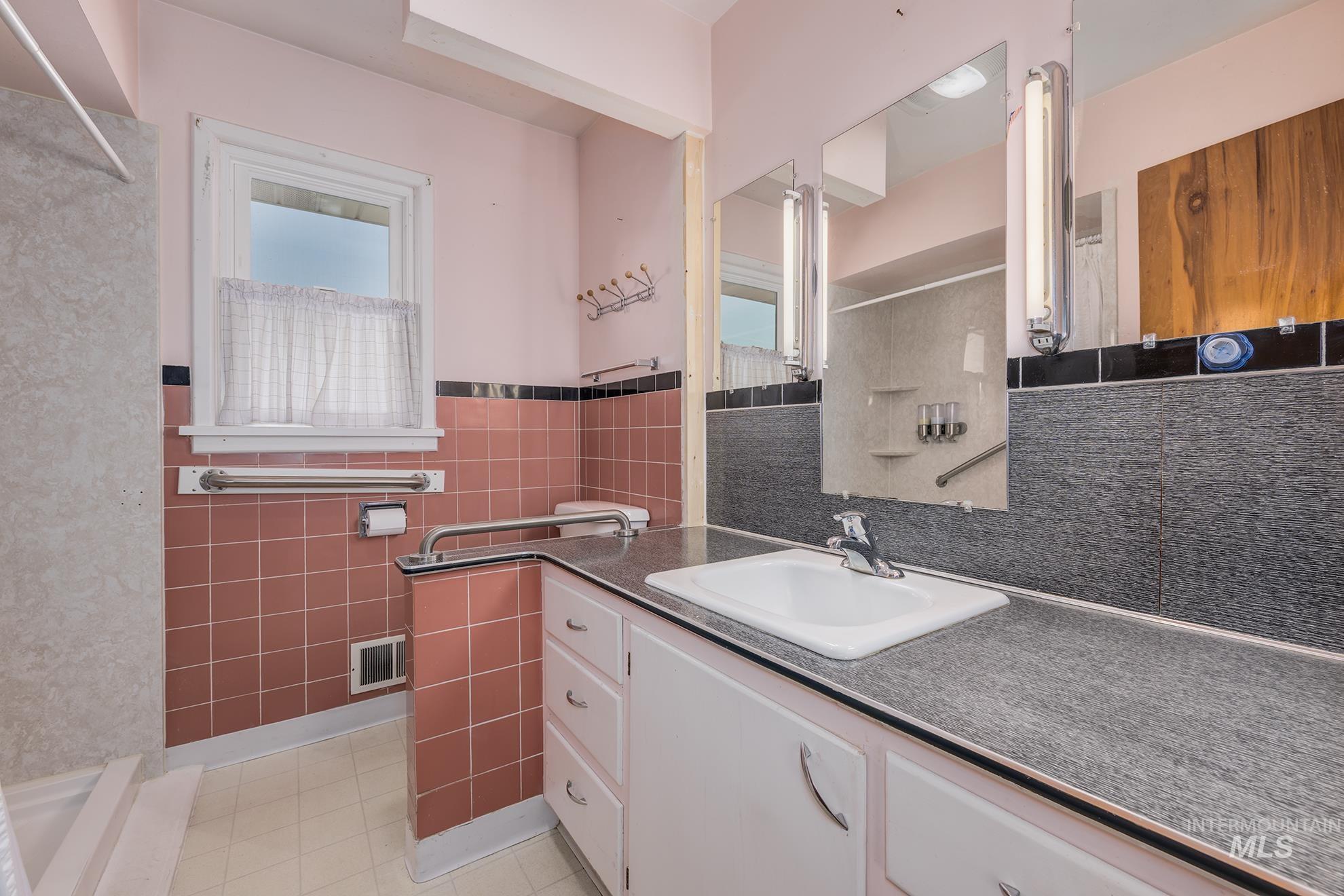 Bathroom featuring tile walls, vanity, a shower, wainscoting, and light tile patterned floors