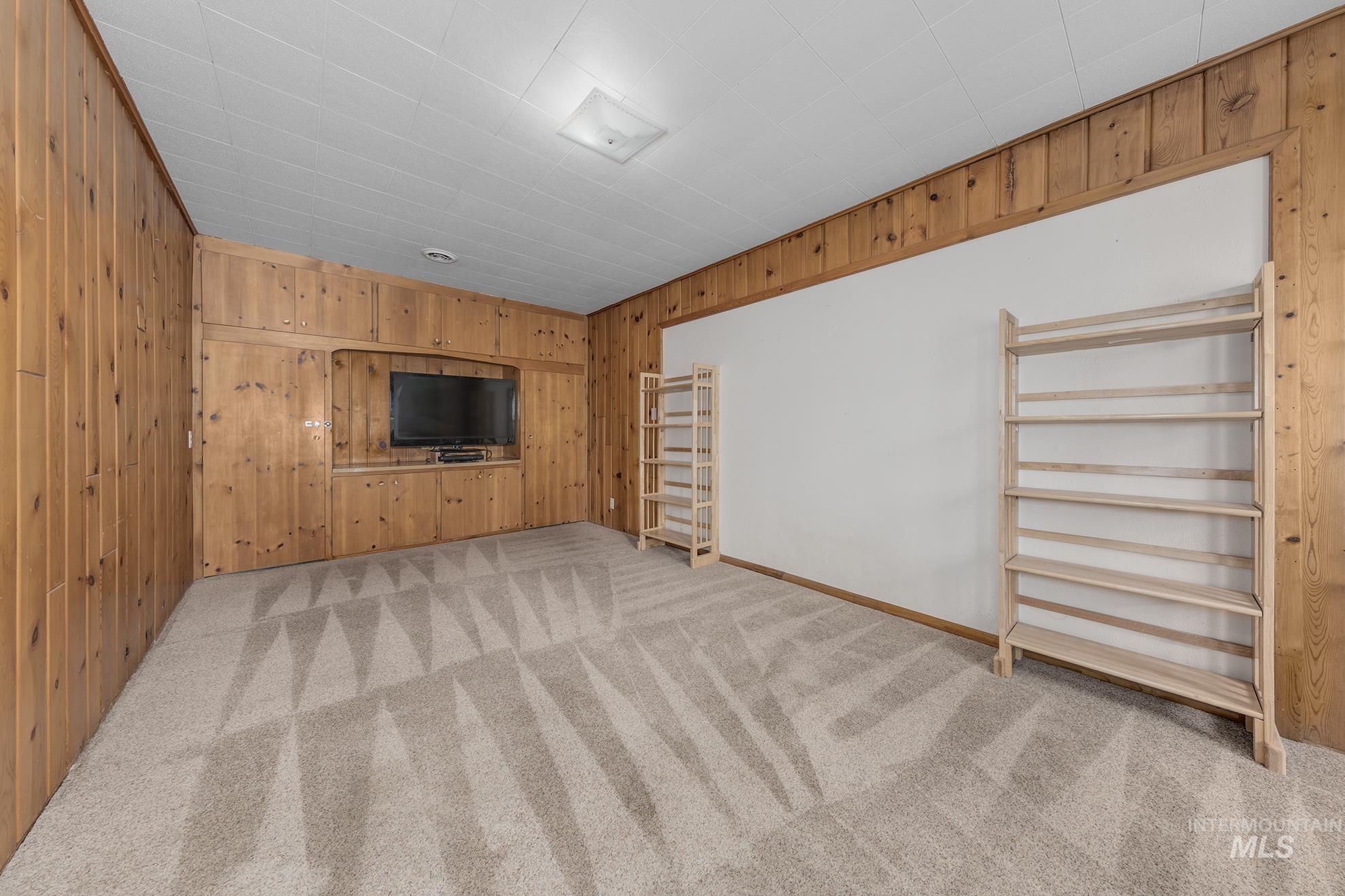 Unfurnished living room with light colored carpet and wood walls