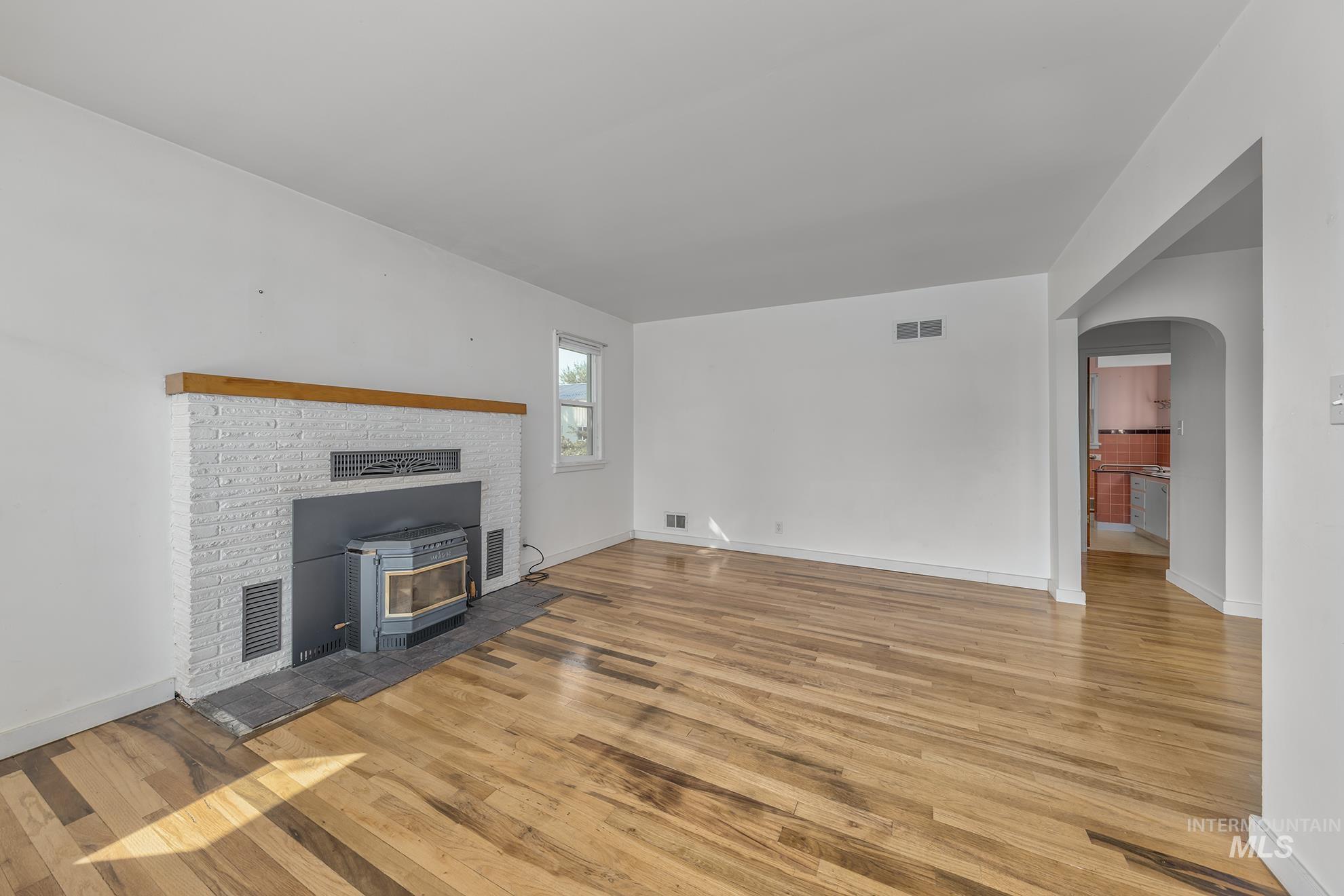 Unfurnished living room featuring arched walkways, light wood finished floors, and a wood stove