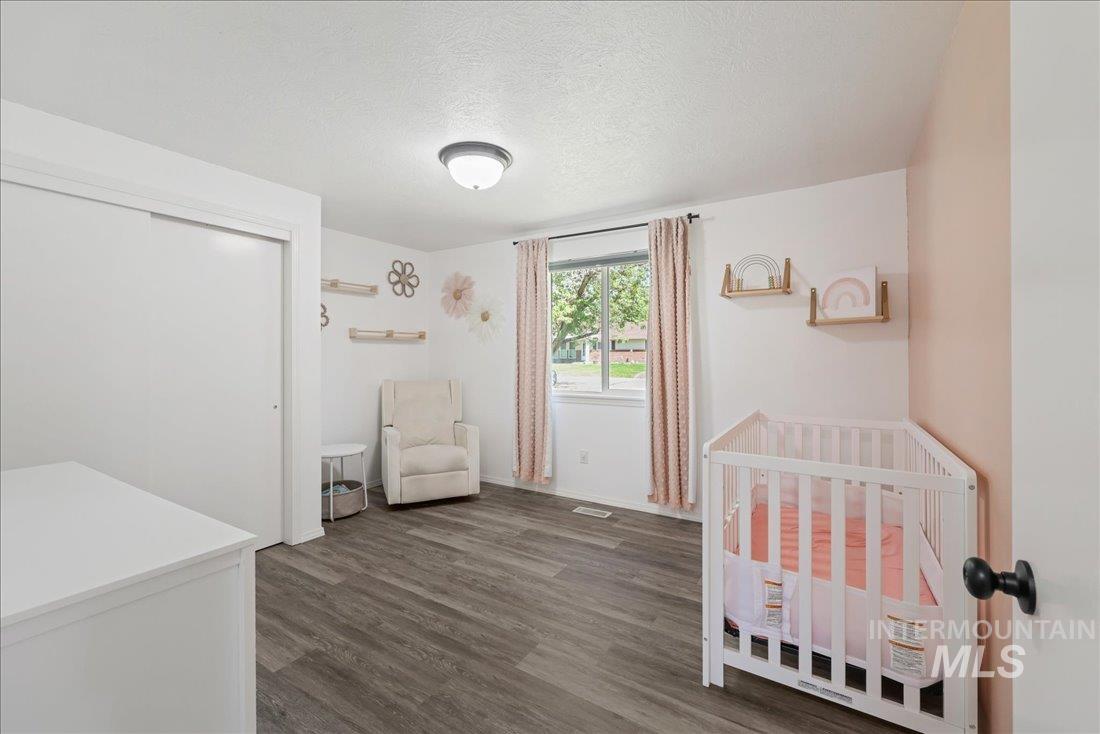 Bedroom featuring a nursery area, a textured ceiling, dark wood-style floors, and a closet