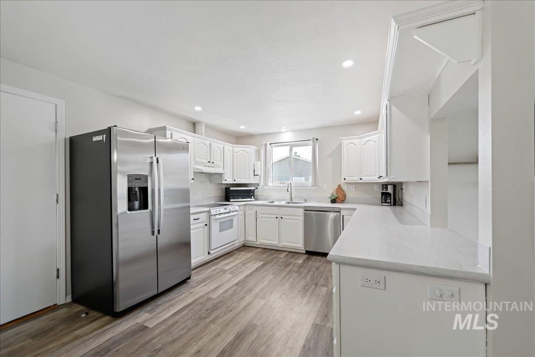 Kitchen with stainless steel appliances, light wood-style floors, white cabinets, recessed lighting, and light stone countertops