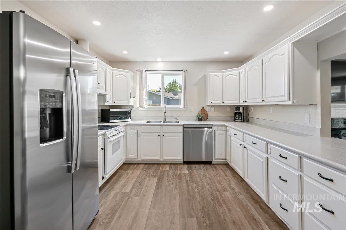 Kitchen with stainless steel appliances, light countertops, white cabinetry, light wood-type flooring, and recessed lighting
