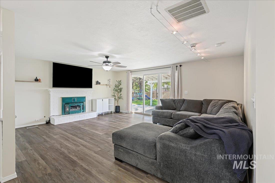 Living area featuring wood finished floors, a glass covered fireplace, a textured ceiling, and a ceiling fan