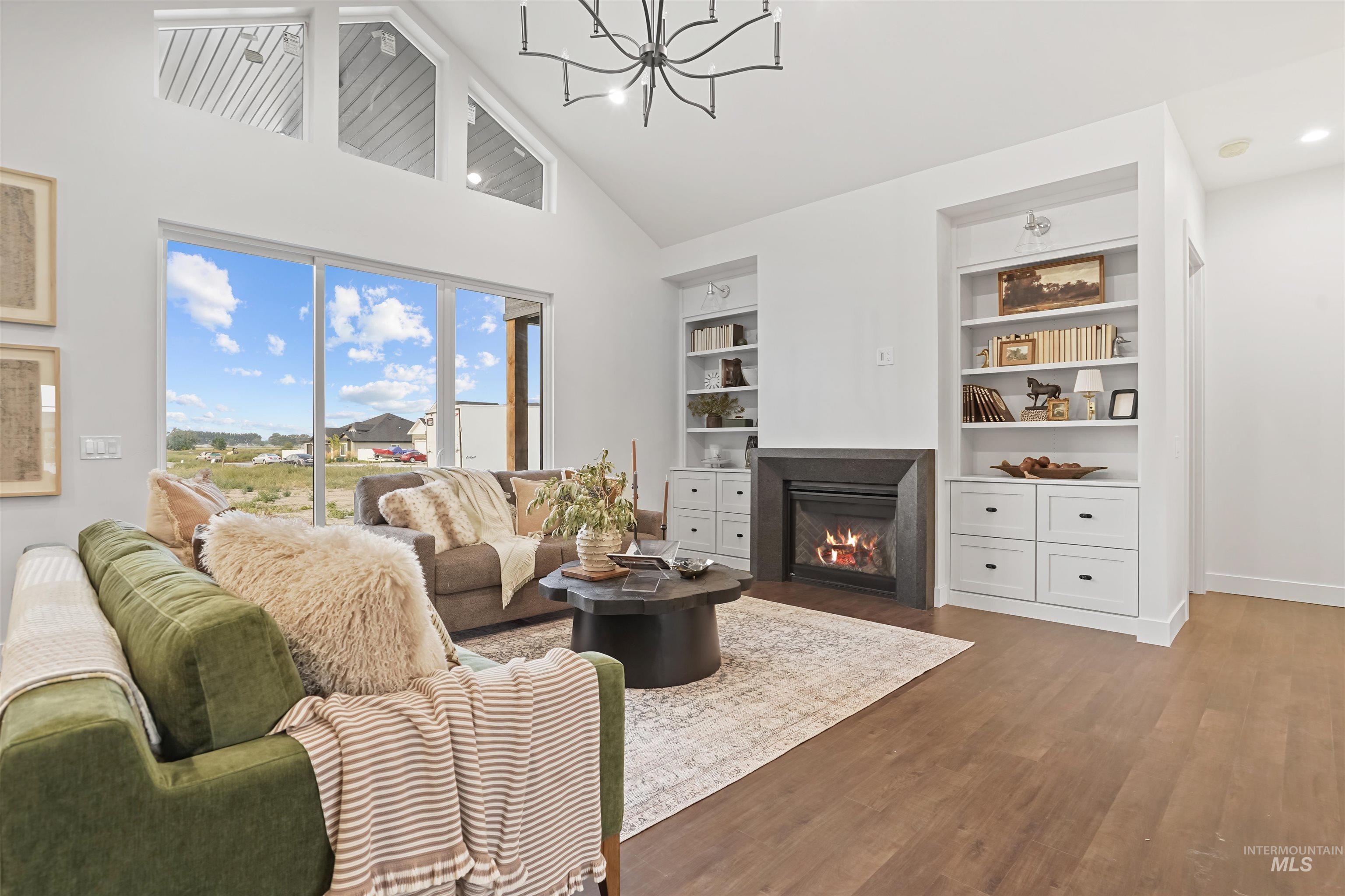 Living room featuring high vaulted ceiling, a fireplace with flush hearth, wood finished floors, built in shelves, and a chandelier