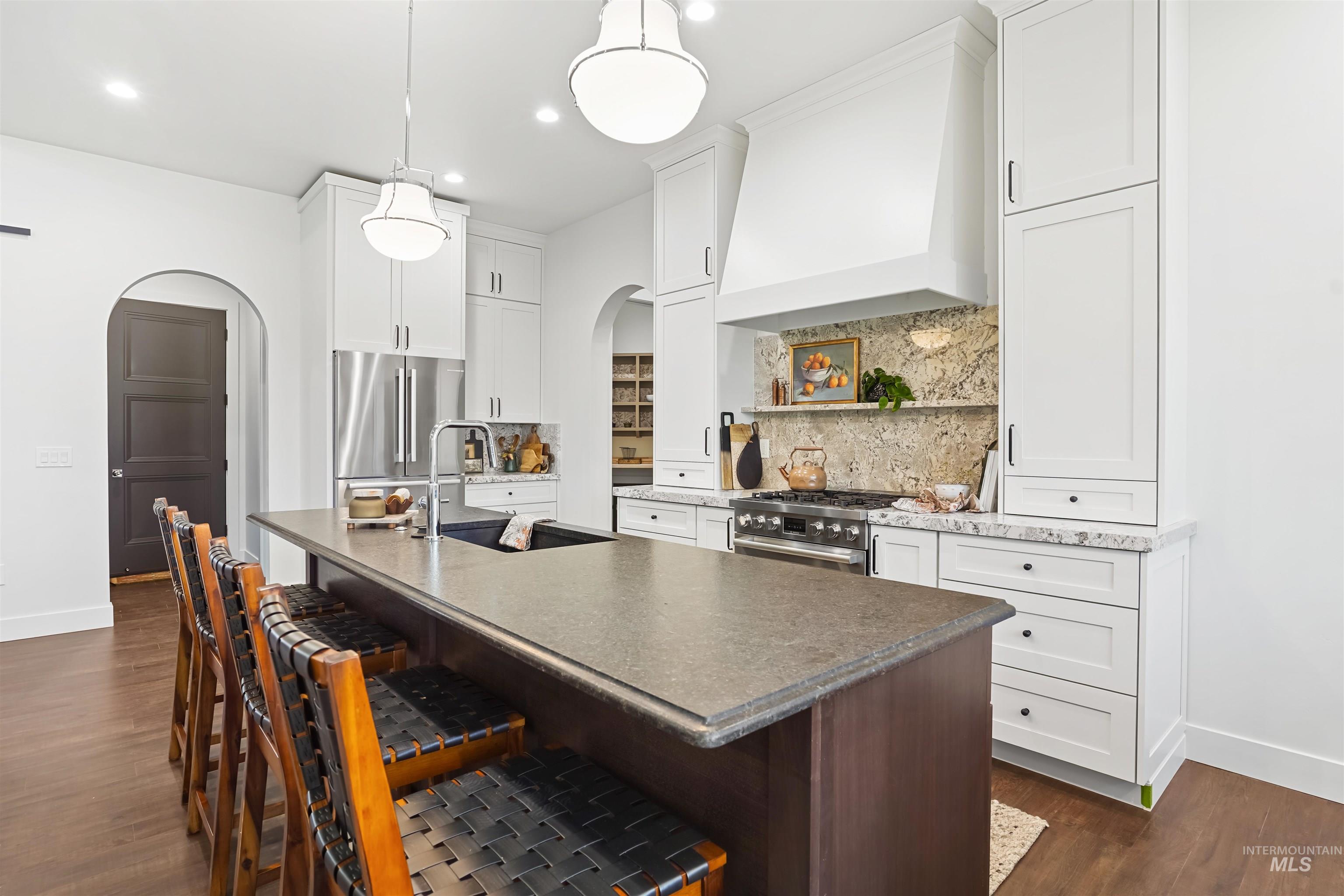 Kitchen featuring arched walkways, decorative backsplash, a kitchen bar, dark wood finished floors, and premium range hood