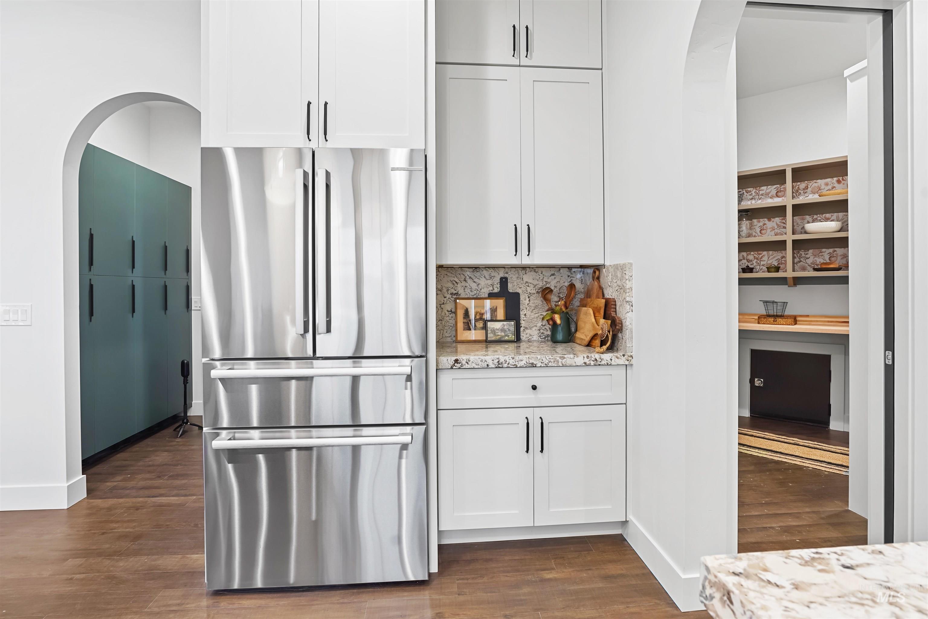 Kitchen featuring arched walkways, freestanding refrigerator, white cabinetry, and light stone counters