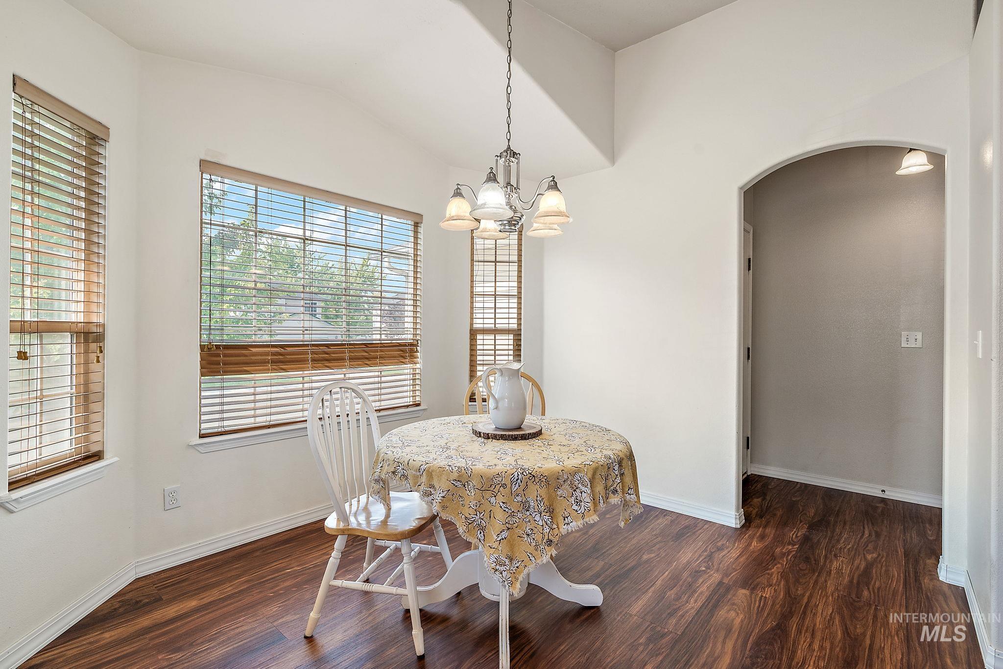 Dining space with arched walkways, dark wood-style flooring, a chandelier, and vaulted ceiling