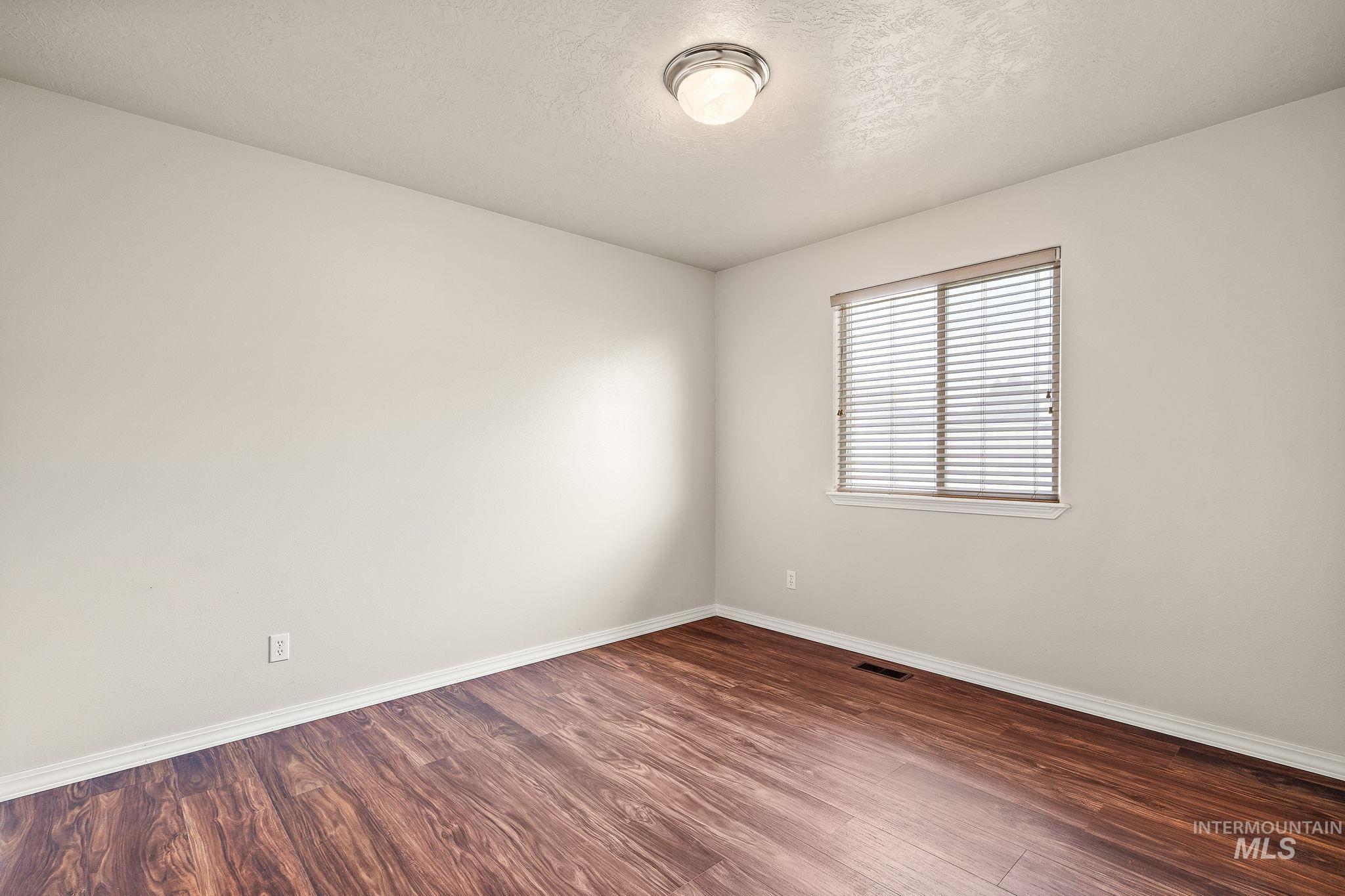 Empty room with a textured ceiling and dark wood-type flooring