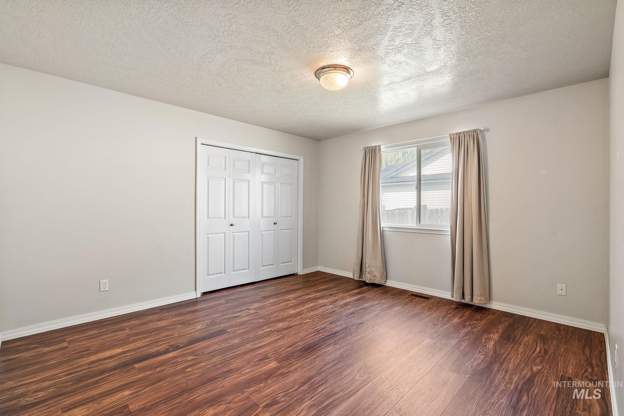 Unfurnished bedroom featuring a textured ceiling, dark wood-style flooring, and a closet