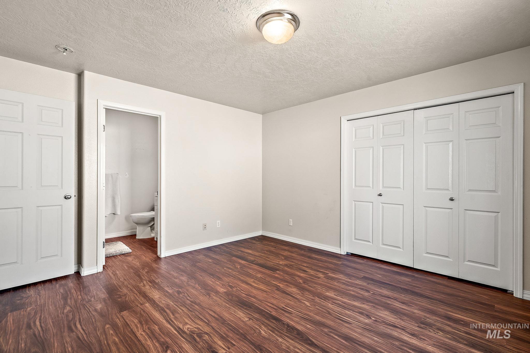 Unfurnished bedroom featuring a textured ceiling, dark wood-style floors, a closet, and ensuite bath
