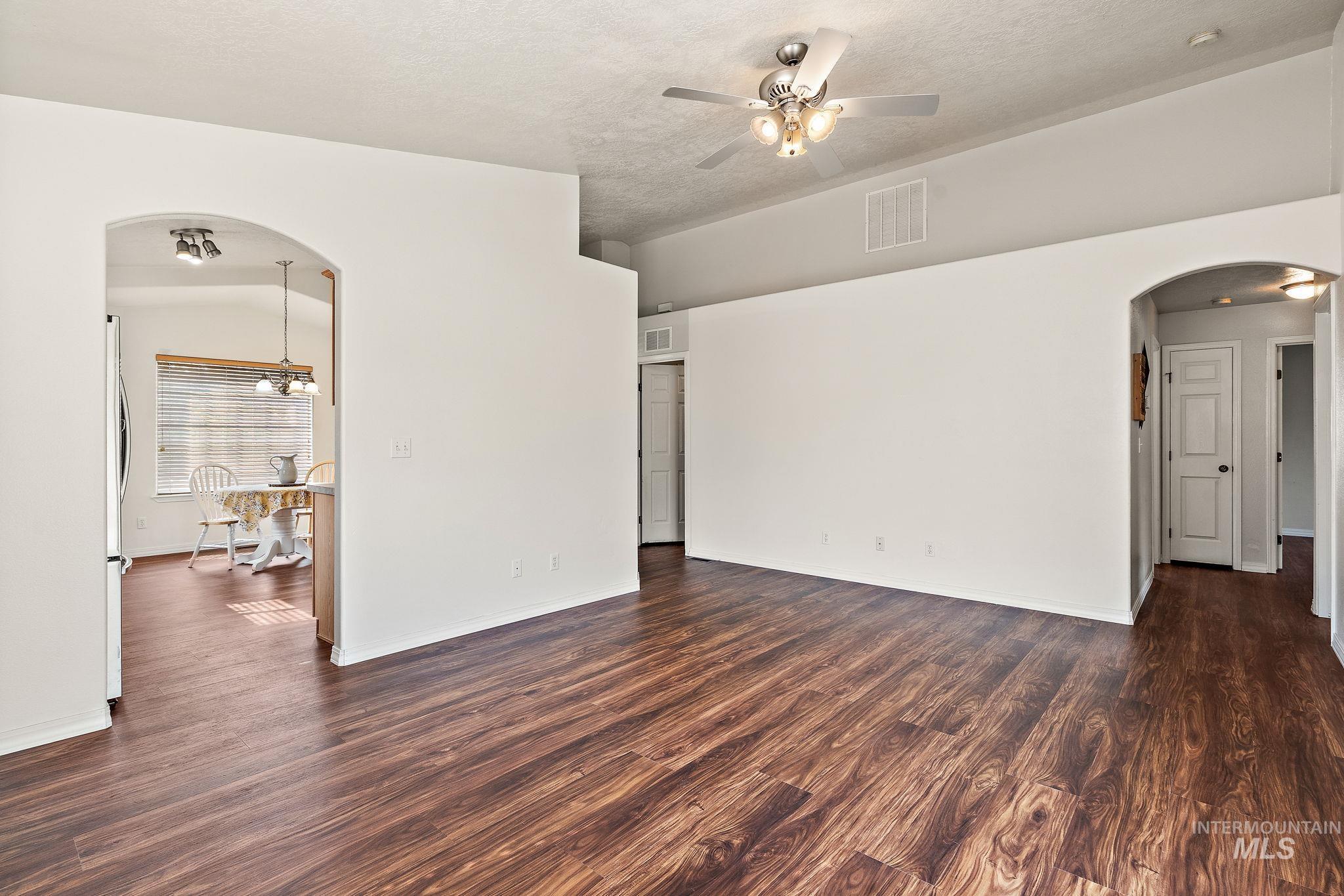 Unfurnished room featuring arched walkways, dark wood finished floors, ceiling fan, and a textured ceiling