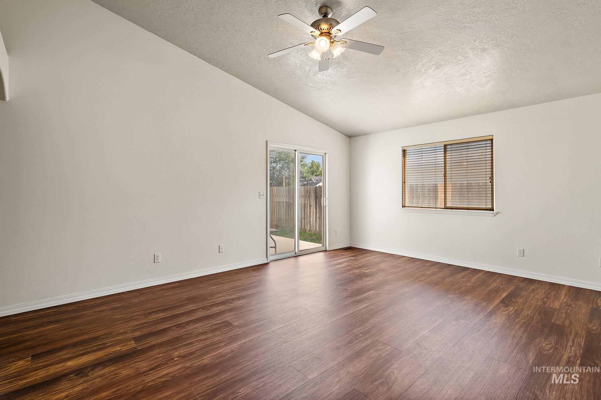 Unfurnished room with a textured ceiling, vaulted ceiling, dark wood-style flooring, and a ceiling fan