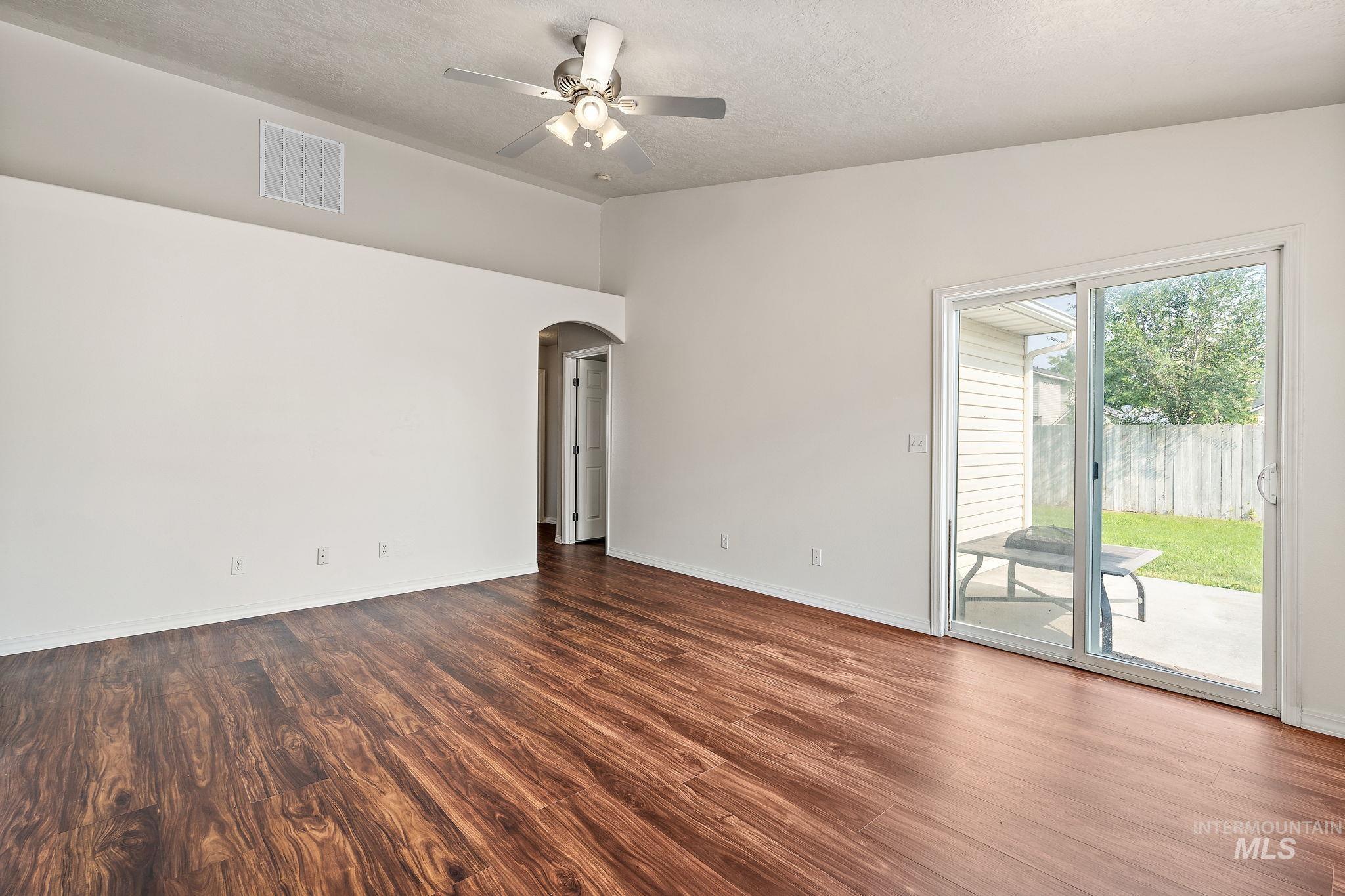 Spare room featuring arched walkways, dark wood-type flooring, a textured ceiling, and a ceiling fan