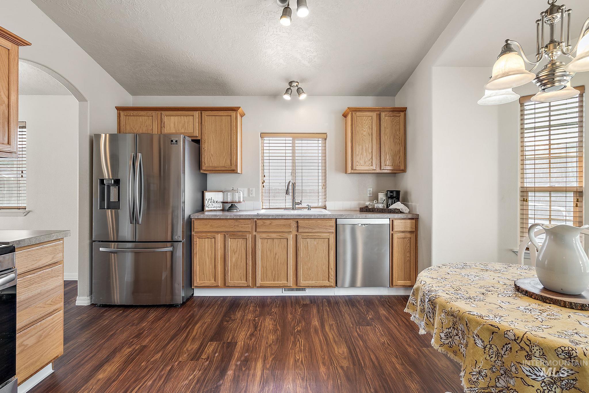 Kitchen featuring appliances with stainless steel finishes, dark wood-style flooring, arched walkways, a textured ceiling, and light countertops