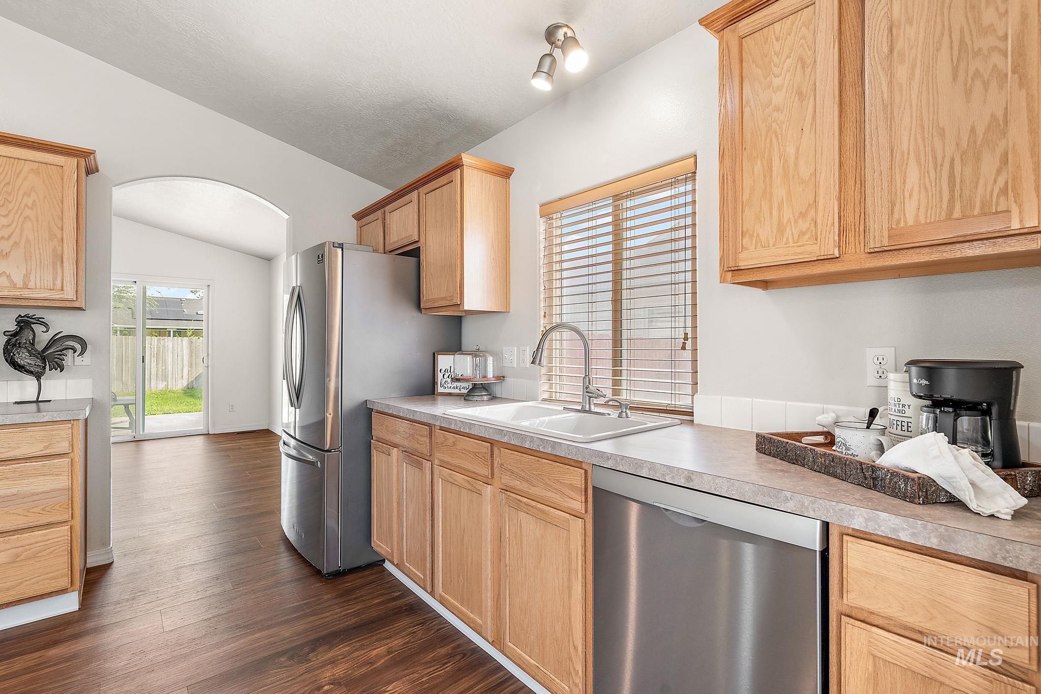 Kitchen with arched walkways, appliances with stainless steel finishes, dark wood-style floors, plenty of natural light, and lofted ceiling