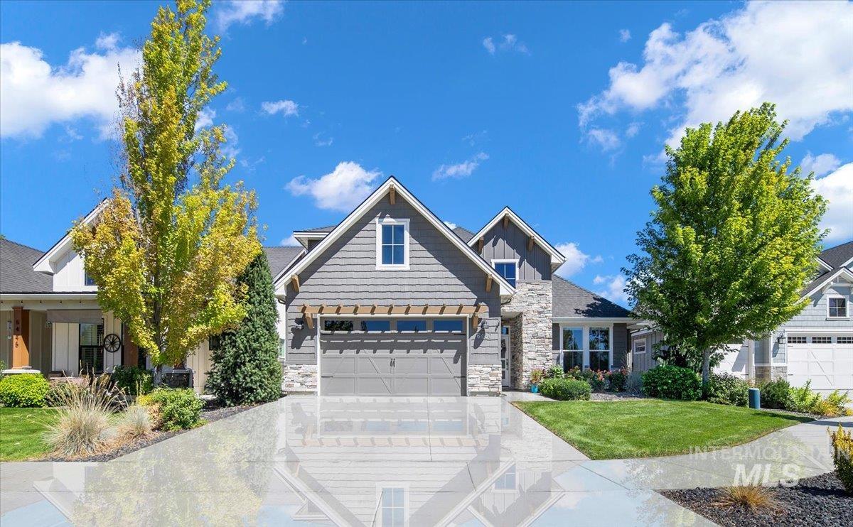 Craftsman-style house with board and batten siding, stone siding, driveway, a garage, and a front lawn