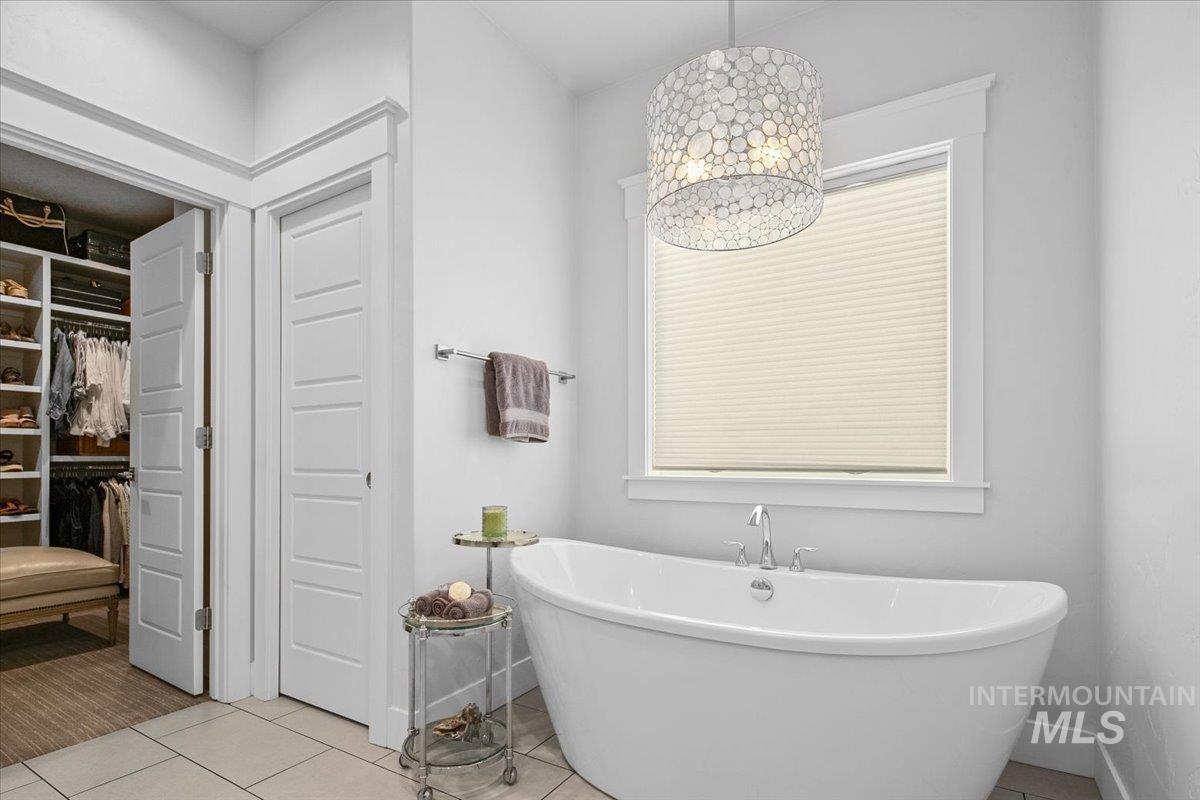 Bathroom featuring a spacious closet, a freestanding tub, and light tile patterned flooring