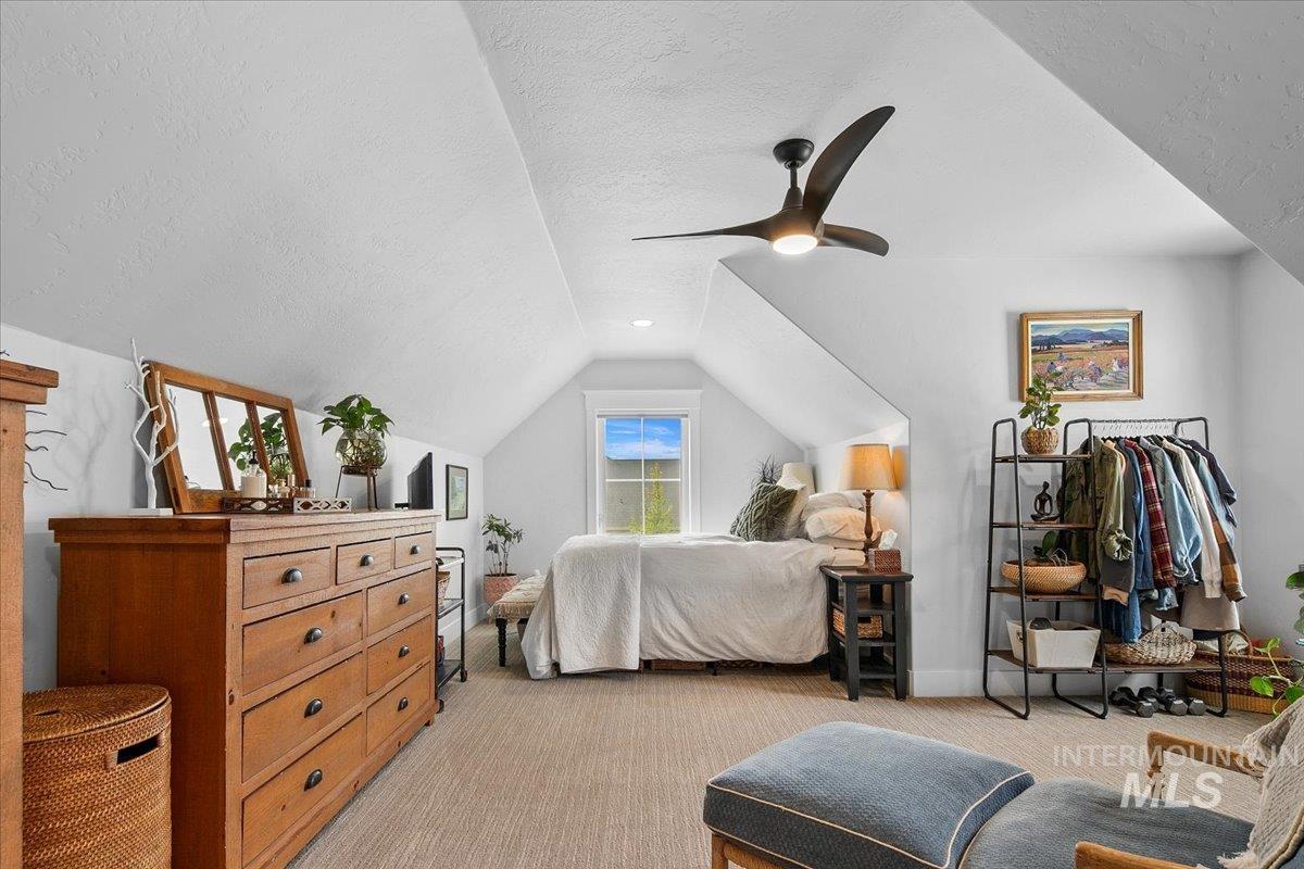 Bedroom featuring a textured ceiling, light colored carpet, lofted ceiling, and ceiling fan
