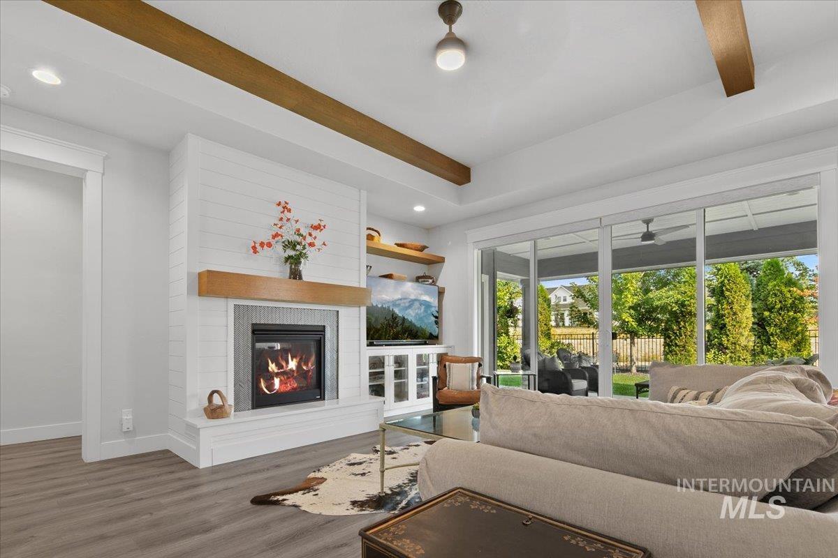 Living area featuring wood finished floors, beam ceiling, recessed lighting, and a glass covered fireplace