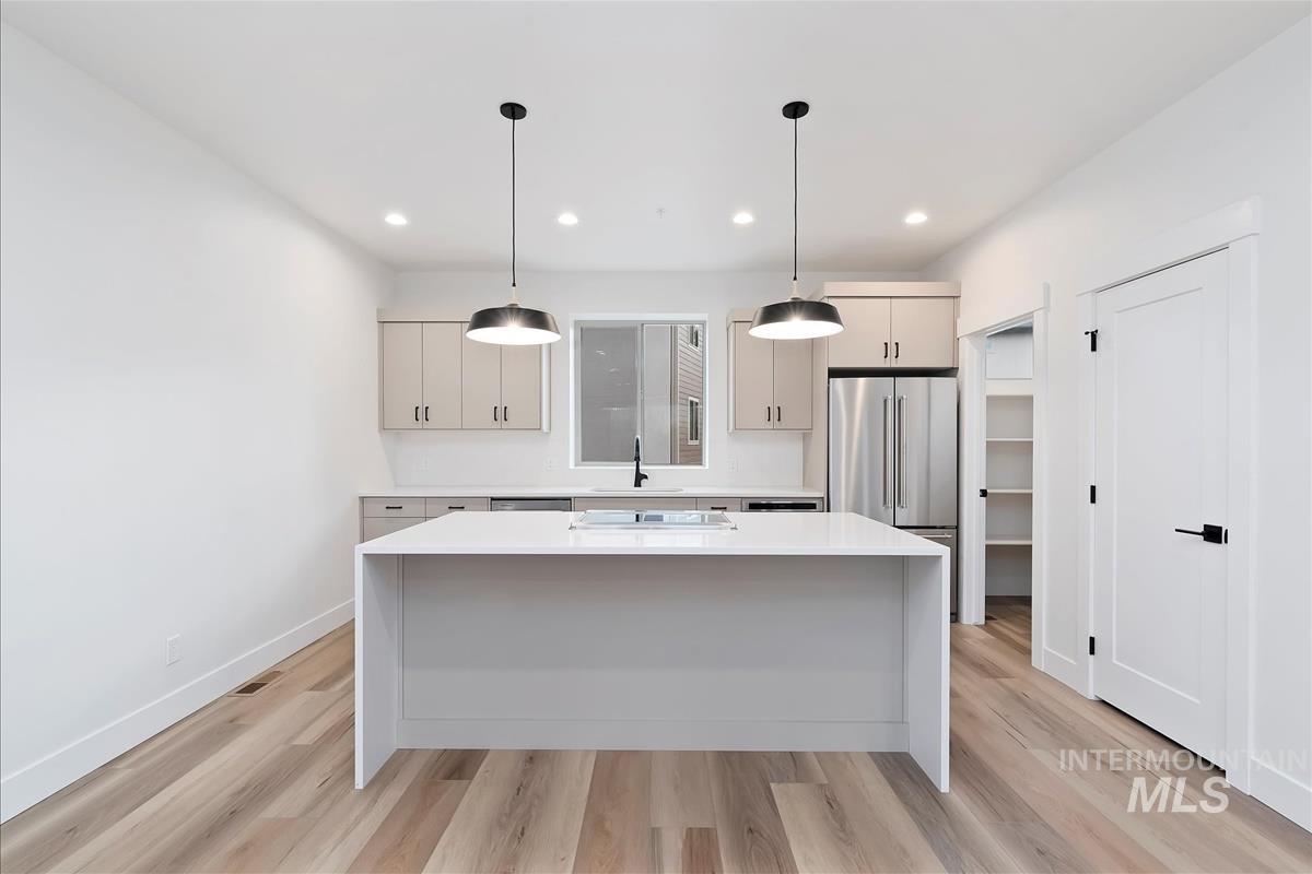 Kitchen with a center island, light stone countertops, light wood-style floors, hanging light fixtures, and freestanding refrigerator