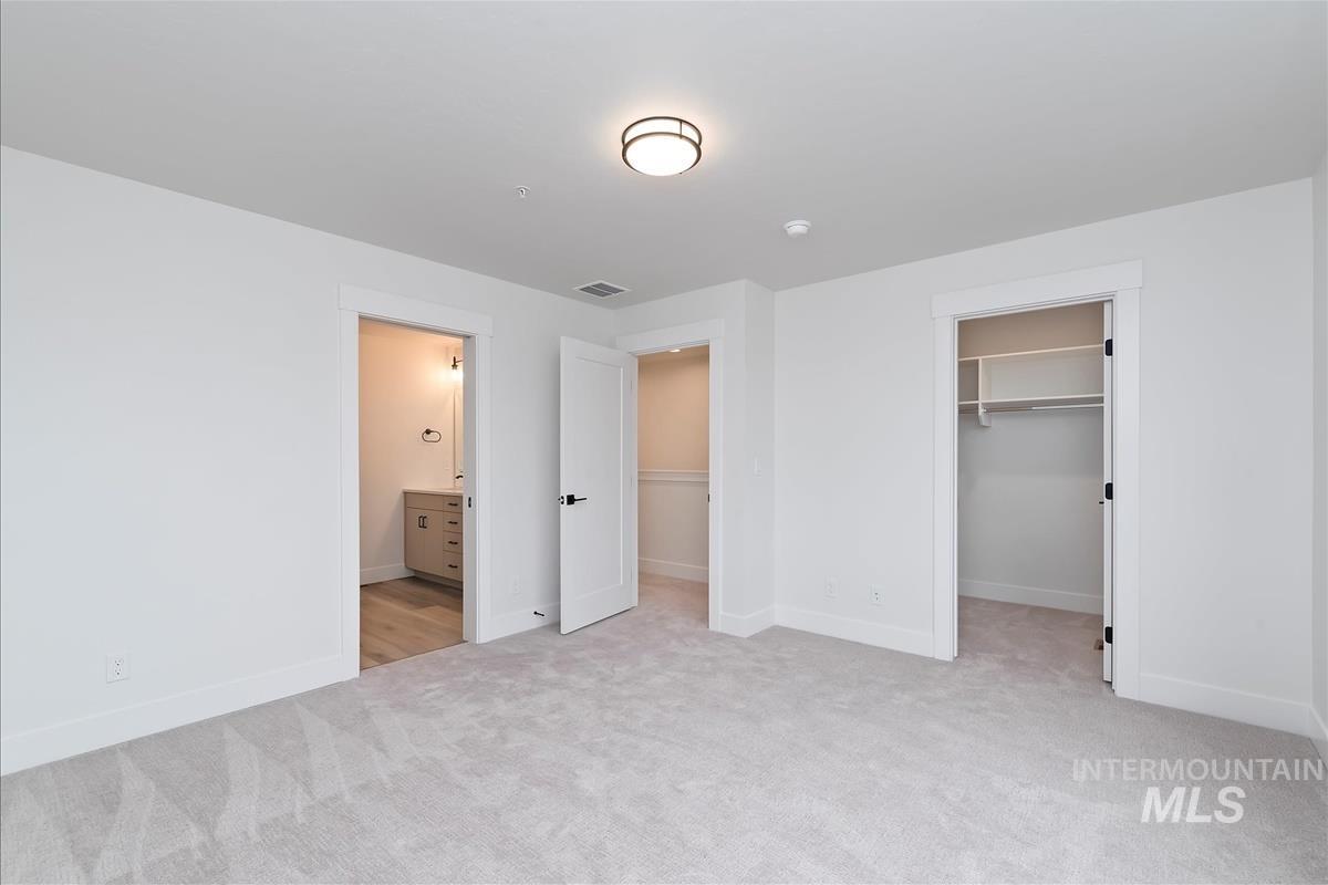 Unfurnished bedroom with a walk in closet, light carpet, and ensuite bathroom