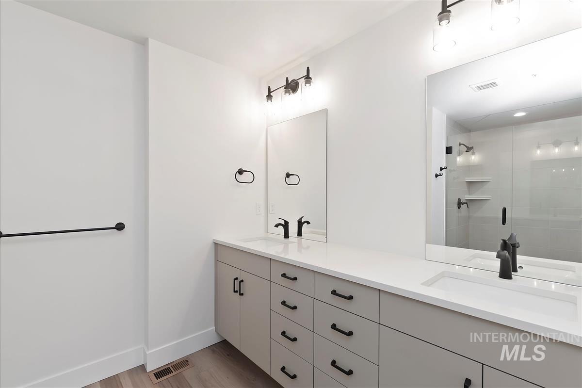 Full bath with double vanity, light wood-type flooring, and a tile shower