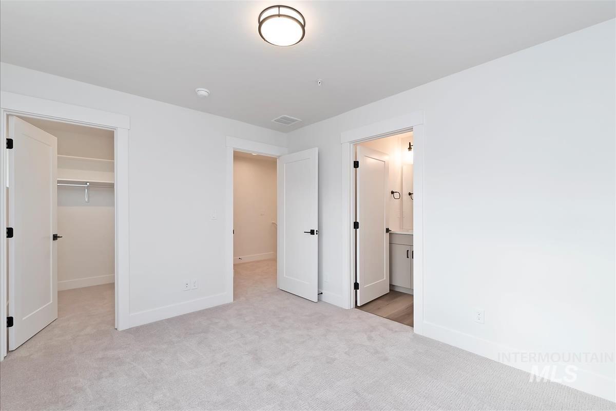 Unfurnished bedroom with a spacious closet, light carpet, and ensuite bathroom