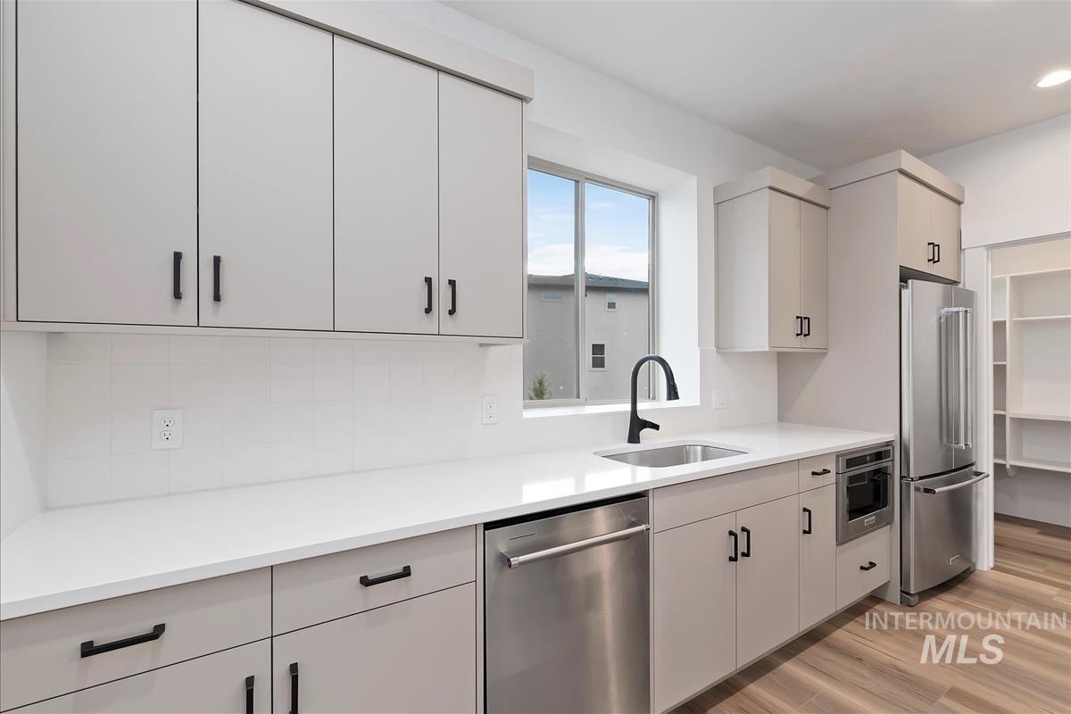 Kitchen with stainless steel appliances, light wood-style floors, backsplash, and white cabinets