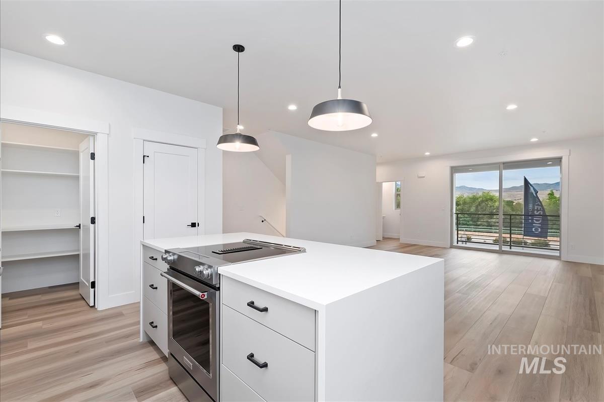 Kitchen with electric stove, white cabinetry, light wood finished floors, hanging light fixtures, and recessed lighting