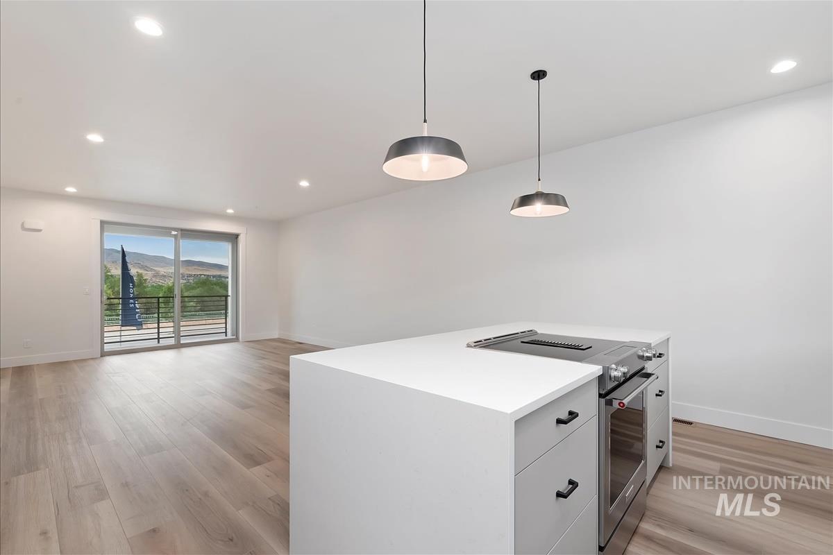 Kitchen featuring stainless steel range, recessed lighting, hanging light fixtures, light wood finished floors, and white cabinets