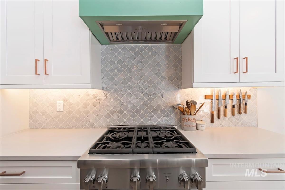Kitchen with exhaust hood, stainless steel gas cooktop, light countertops, and white cabinets