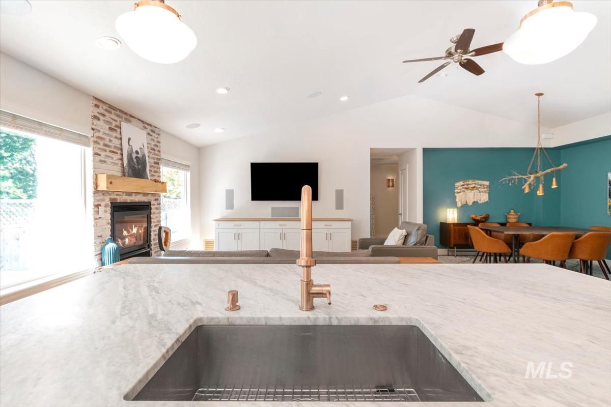 Kitchen featuring open floor plan, lofted ceiling, a brick fireplace, light stone countertops, and ceiling fan