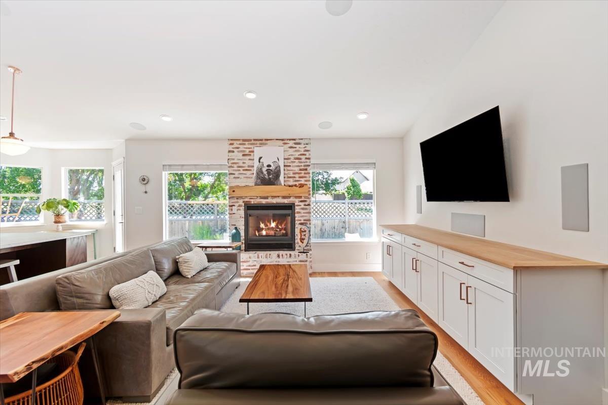 Living room with light wood-type flooring, recessed lighting, a brick fireplace, and lofted ceiling