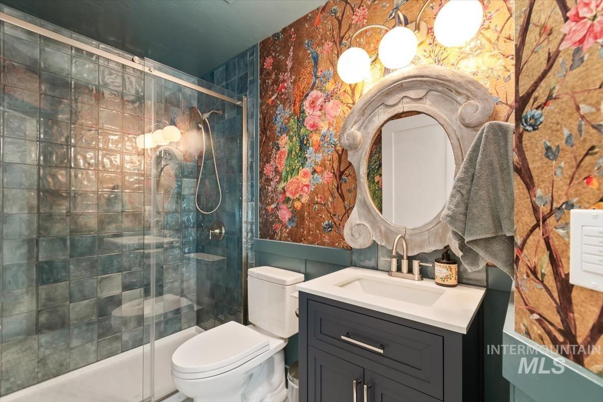 Full bath featuring wallpapered walls, vanity, and a stall shower