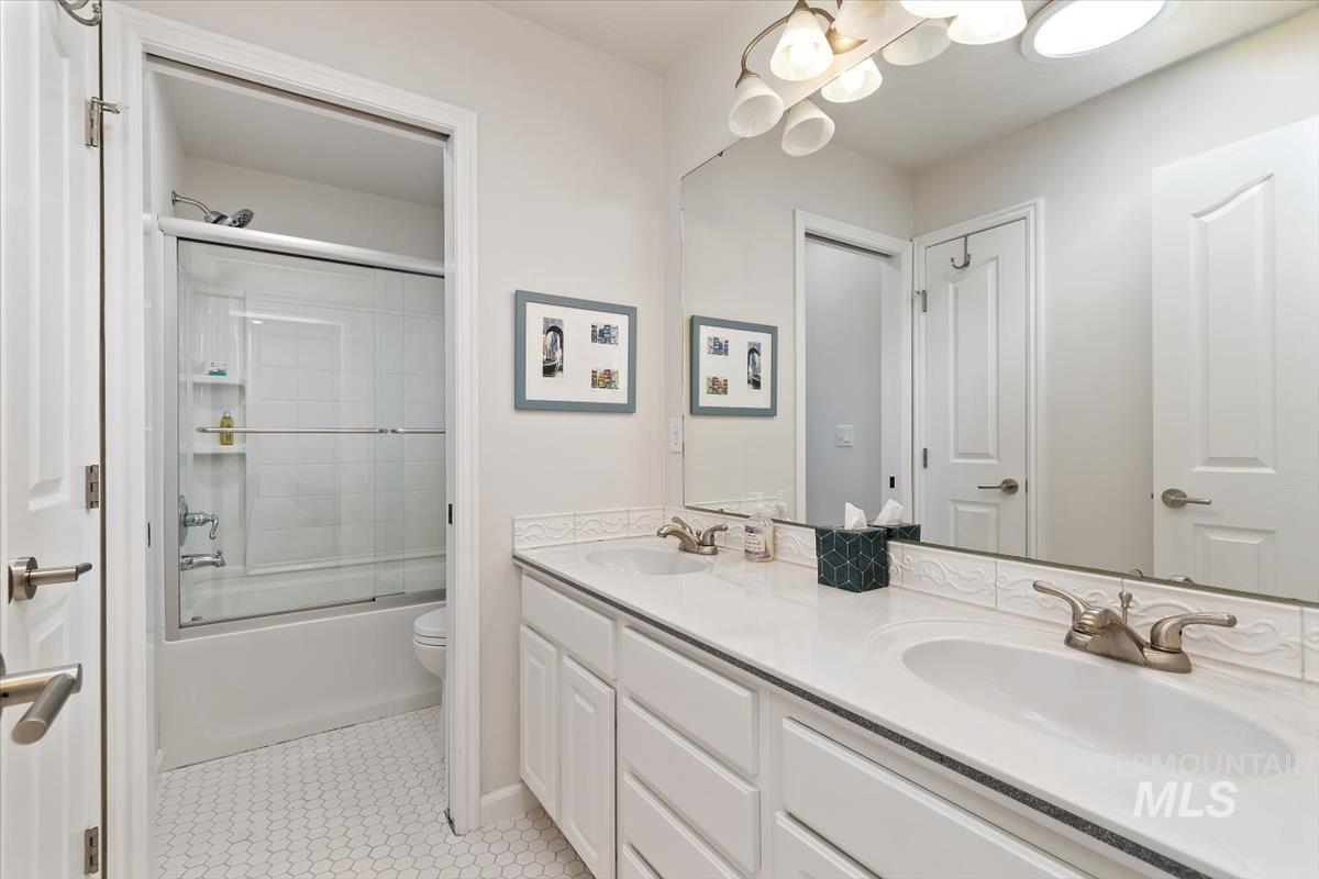 Full bath with double vanity, shower / bath combination with glass door, and tile patterned floors