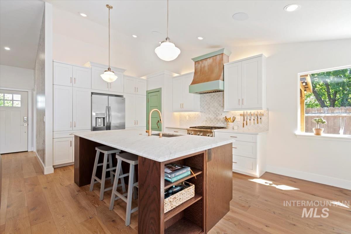 Kitchen featuring lofted ceiling, light wood-type flooring, stainless steel refrigerator with ice dispenser, open shelves, and an island with sink
