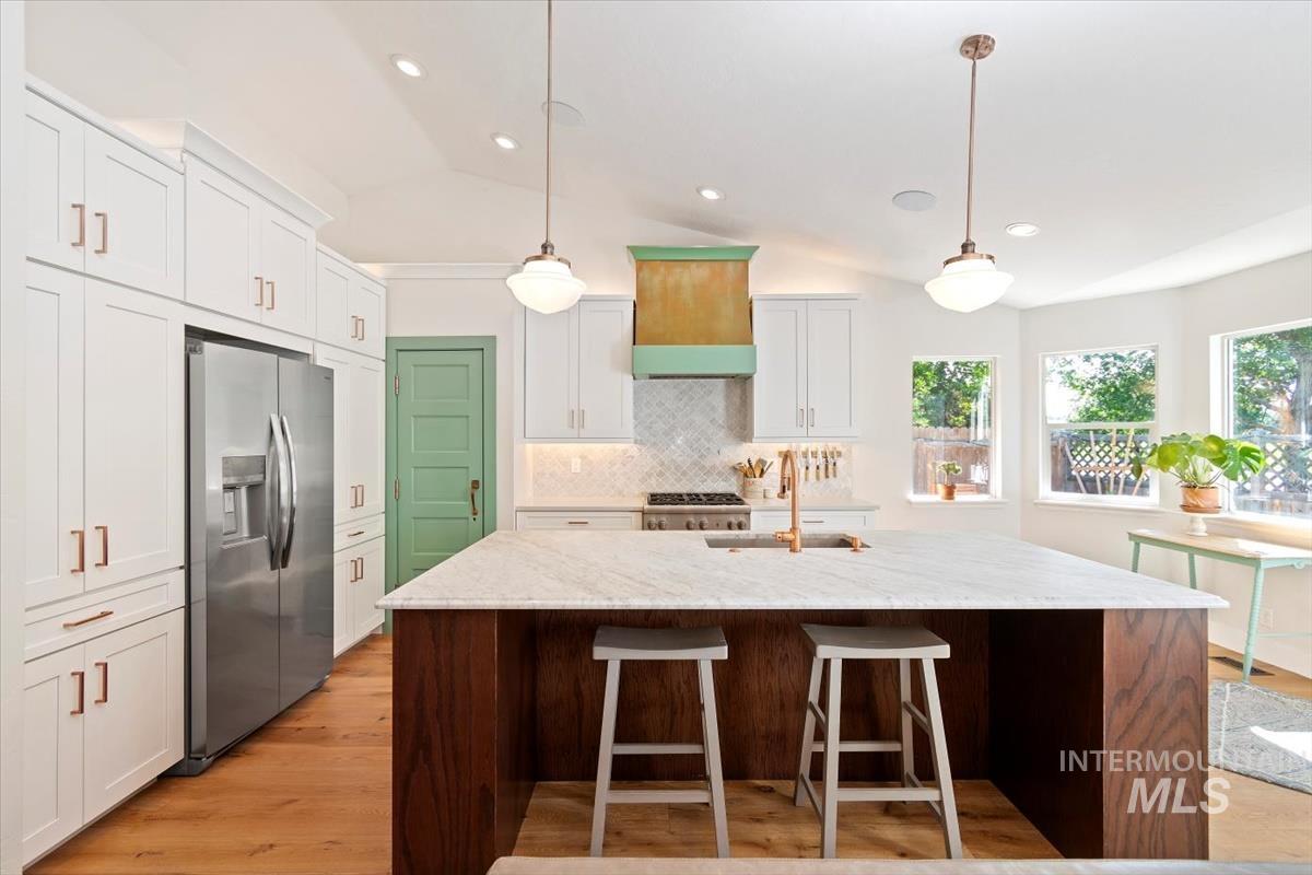 Kitchen featuring lofted ceiling, stainless steel fridge, light wood-type flooring, light stone counters, and decorative backsplash