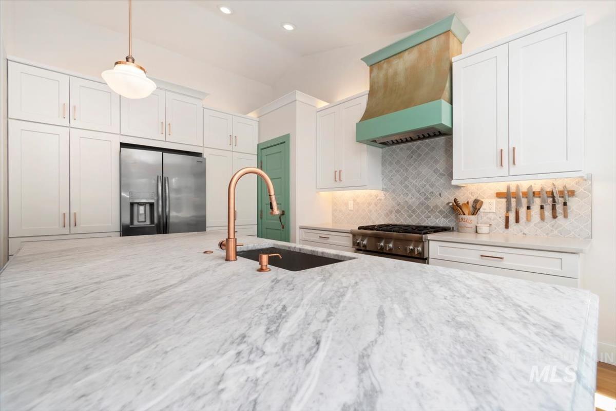 Kitchen with appliances with stainless steel finishes, light stone counters, custom range hood, pendant lighting, and vaulted ceiling