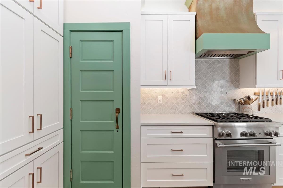 Kitchen featuring high end stainless steel range, custom exhaust hood, white cabinetry, and light countertops