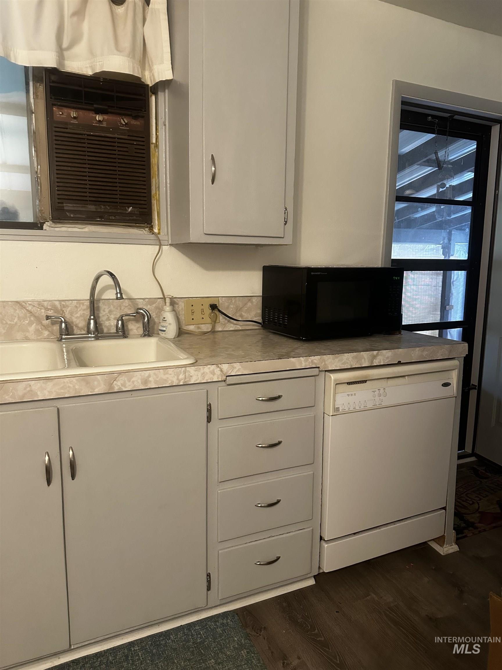 Kitchen featuring dishwasher, black microwave, light countertops, dark wood finished floors, and cooling unit