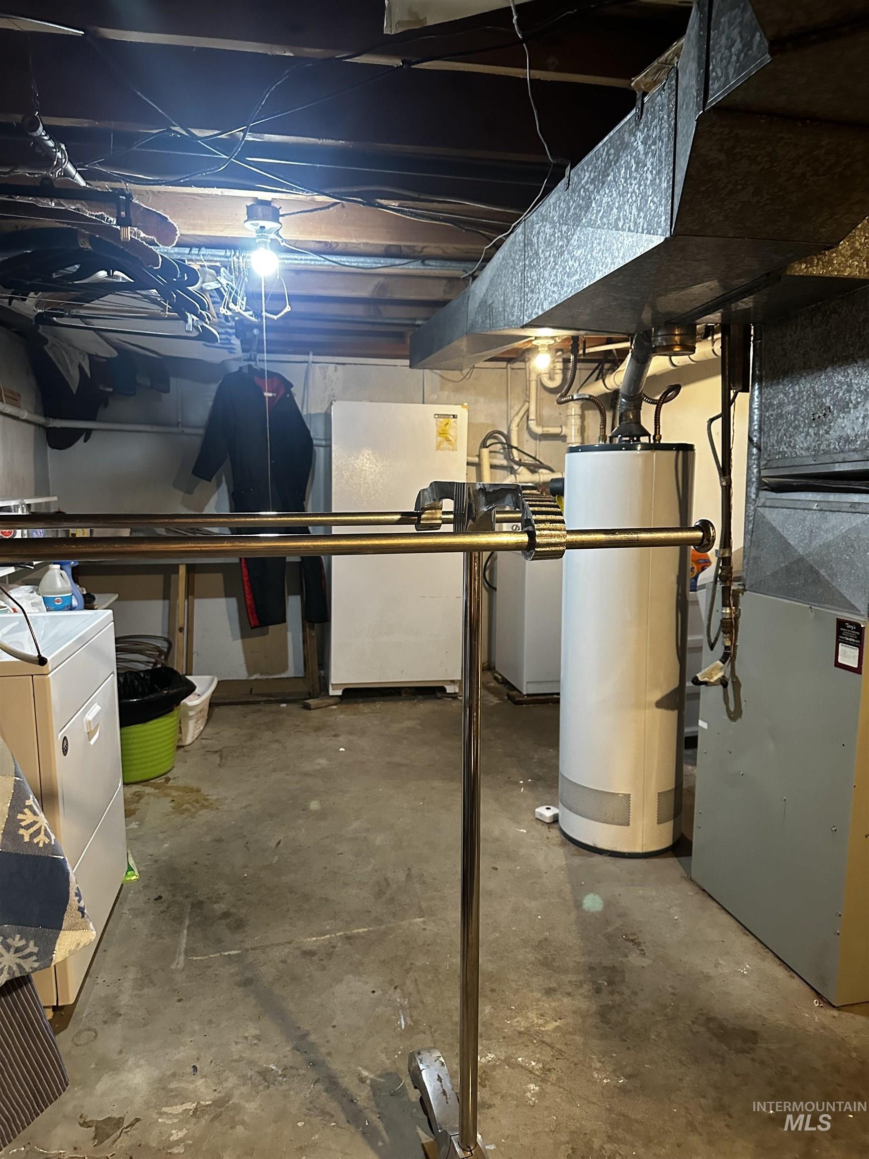 Unfinished below grade area with water heater, freestanding refrigerator, heating unit, and washer / dryer