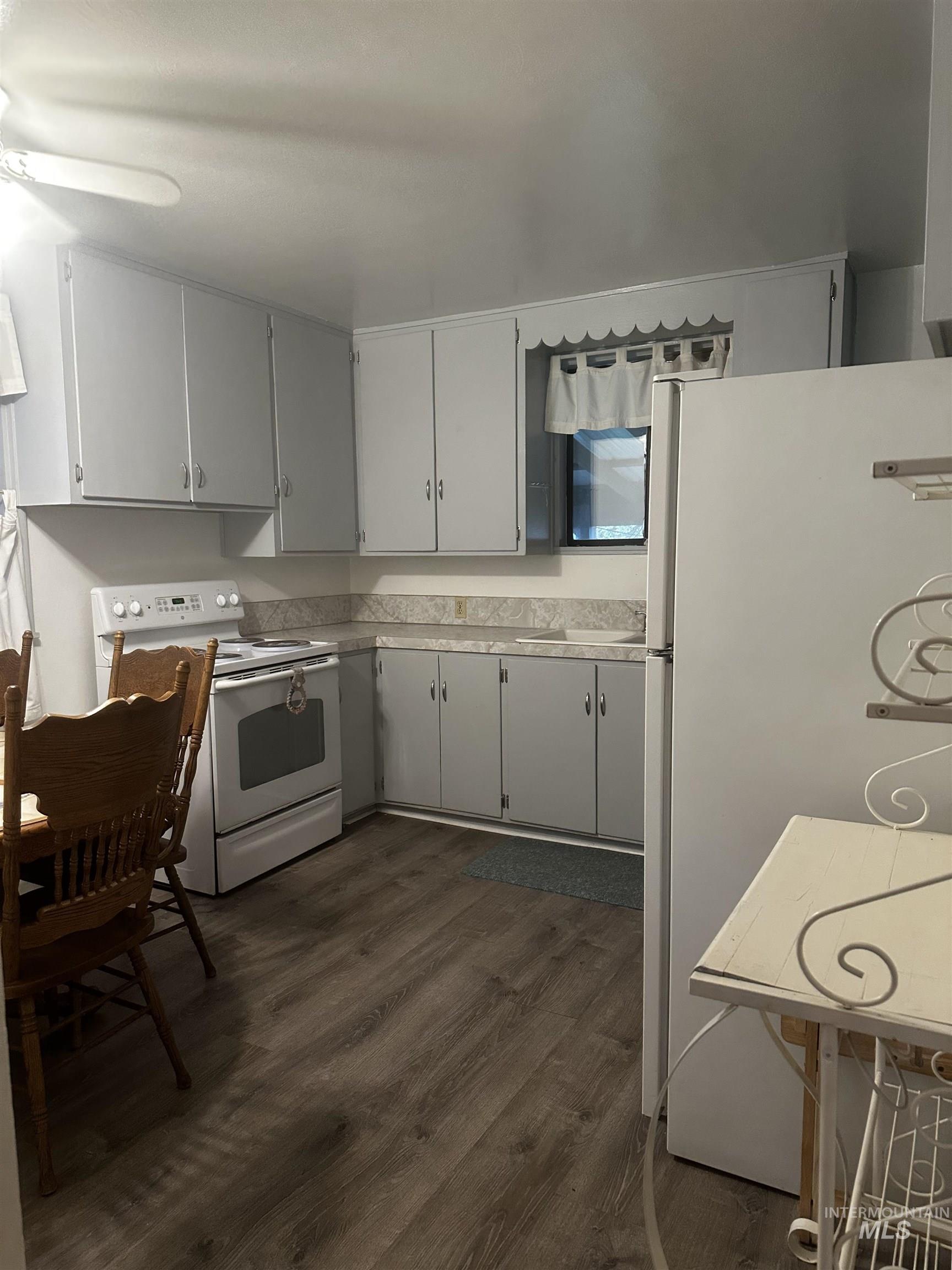 Kitchen featuring white appliances, dark wood-style floors, light countertops, and gray cabinets