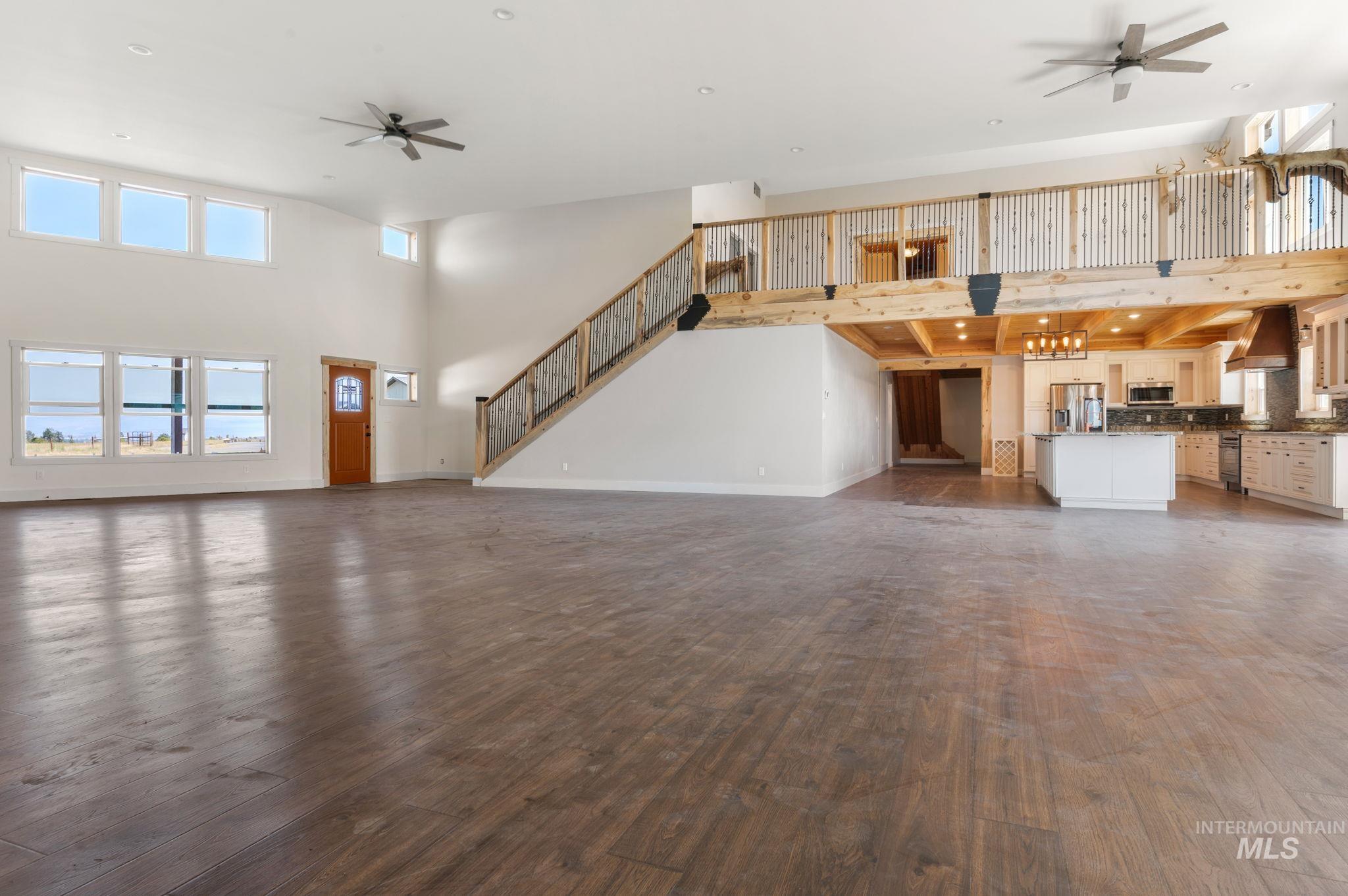Unfurnished living room with a ceiling fan, a towering ceiling, dark wood finished floors, and stairs