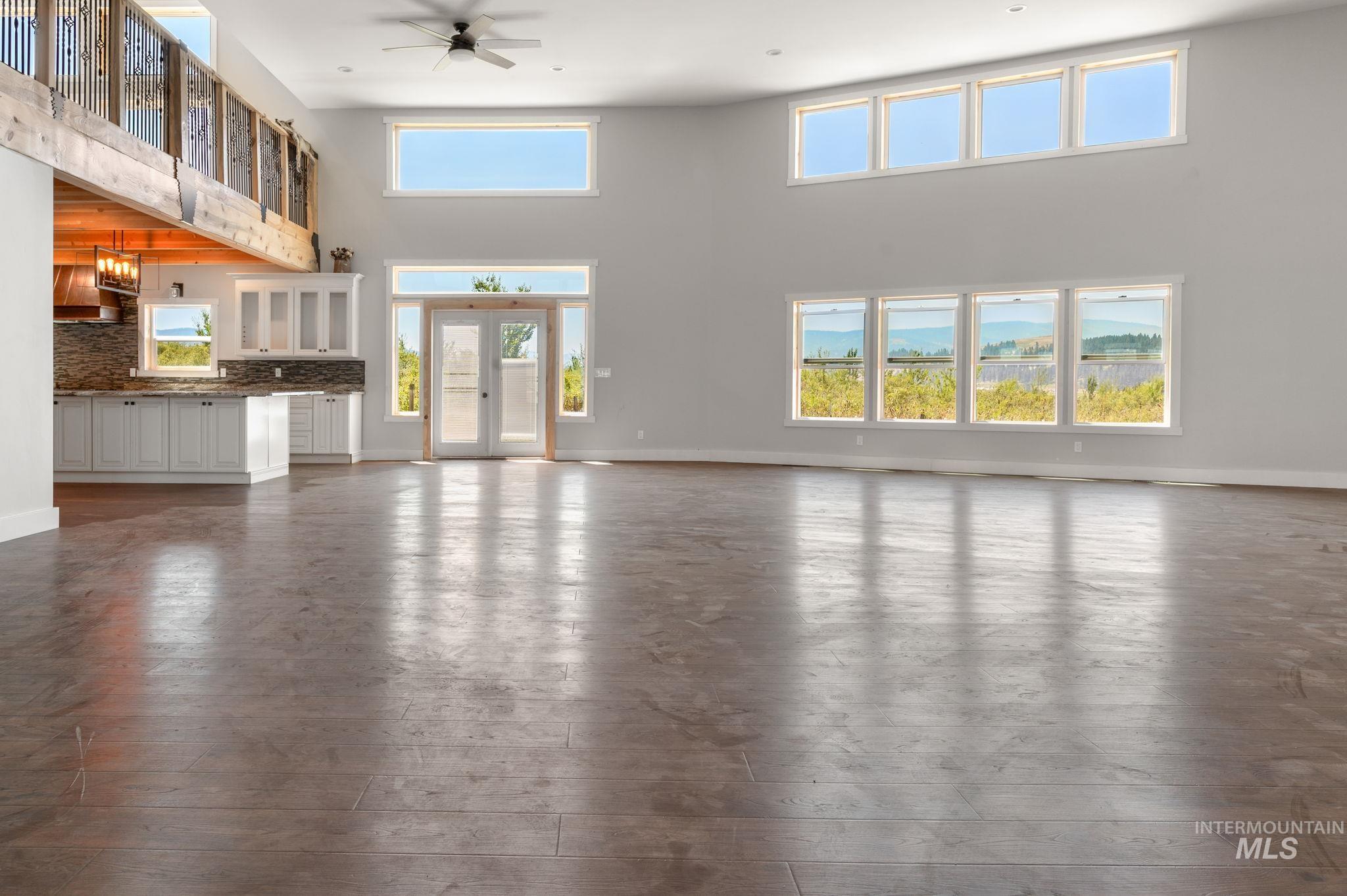 Unfurnished living room featuring a high ceiling, dark wood-style flooring, ceiling fan, and french doors
