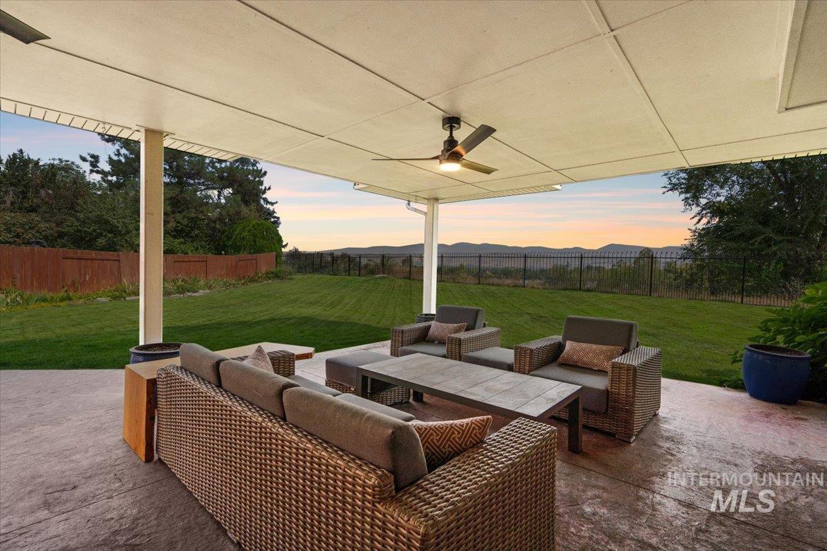 Patio terrace at dusk with a patio area, outdoor lounge area, a fenced backyard, a ceiling fan, and a mountain view