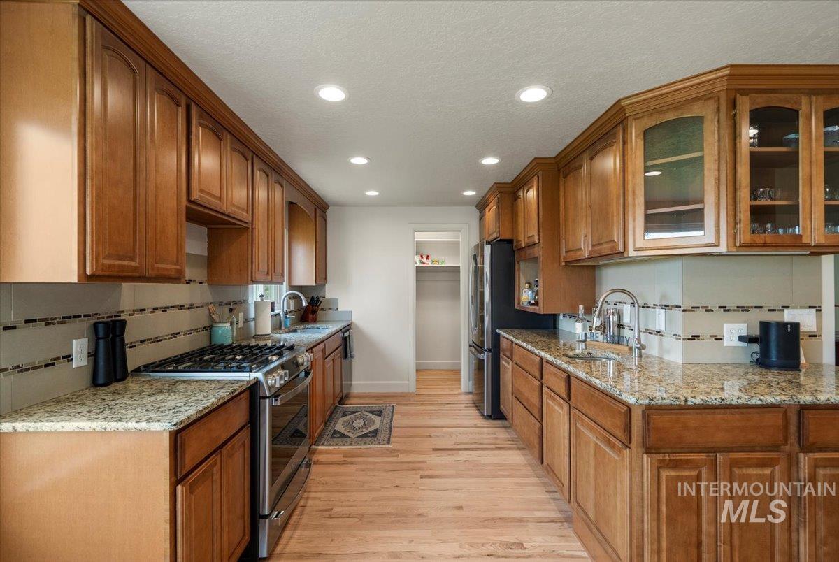 Kitchen featuring backsplash, stainless steel appliances, light stone counters, brown cabinetry, and recessed lighting