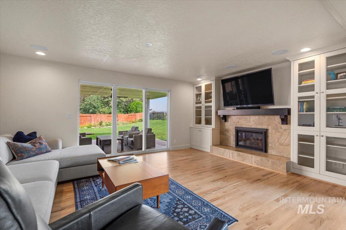 Living area with light wood-type flooring, a glass covered fireplace, built in features, a textured ceiling, and recessed lighting
